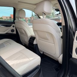 Auto Spa - Jasne, skórzane fotele tylne w czarnym samochodzie SUV, widoczne przez otwarte drzwi. Czyste wnętrze, dywaniki gumowe. Widok na zewnątrz przez okno.