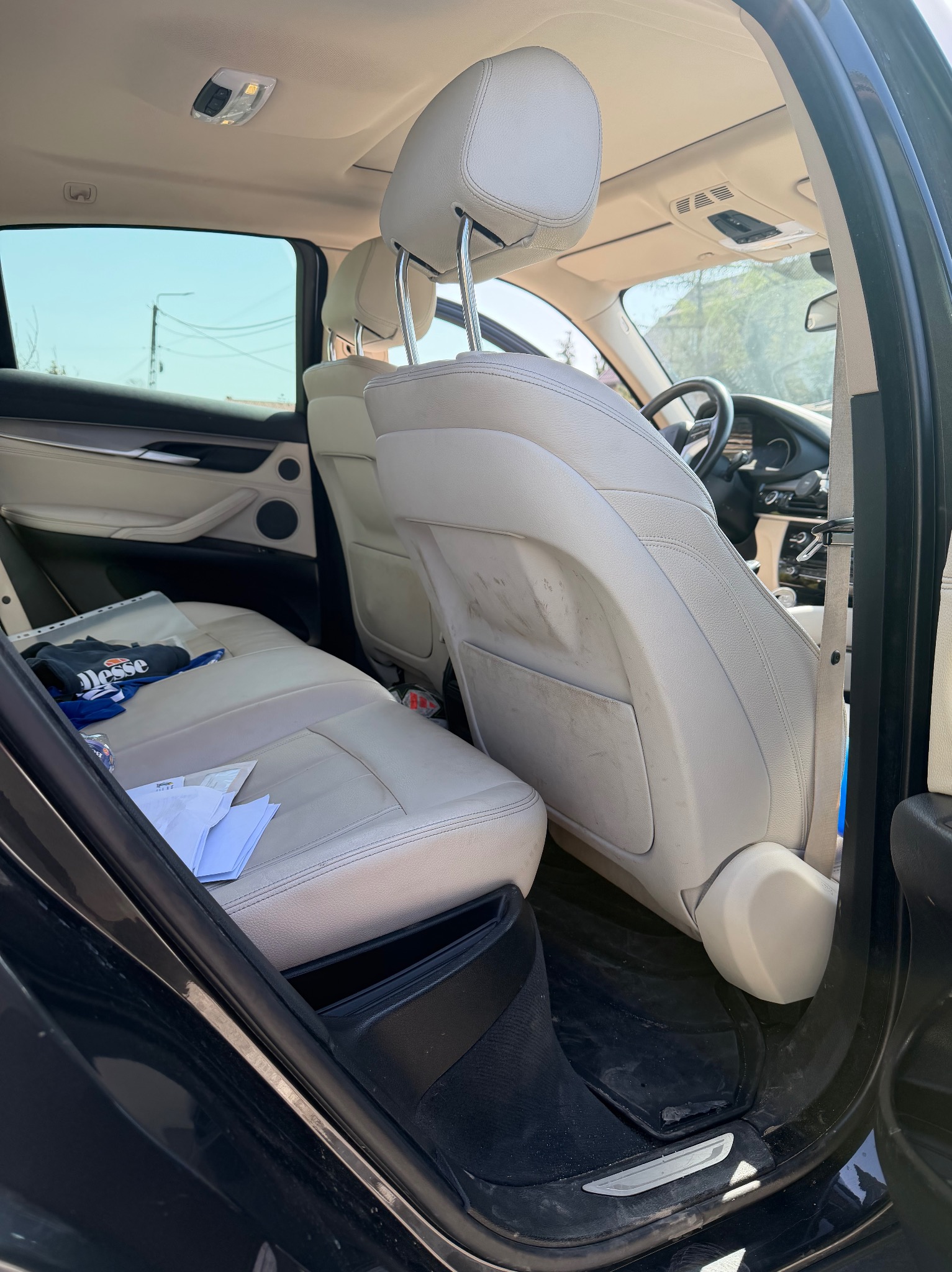 Wnętrze samochodu z jasną, zabrudzoną tapicerką skórzaną na tylnych siedzeniach. Widoczne ślady użytkowania i zabrudzenia na oparciu fotela. Na siedzeniu leżą dokumenty i bluza.