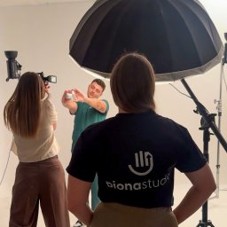 PIONA Studio Oskar Makarski - Sesja zdjęciowa w studio: mężczyzna w zielonym stroju prezentuje produkt, fotografka robi zdjęcia, a osoba z logo 'bionastudio' obserwuje.