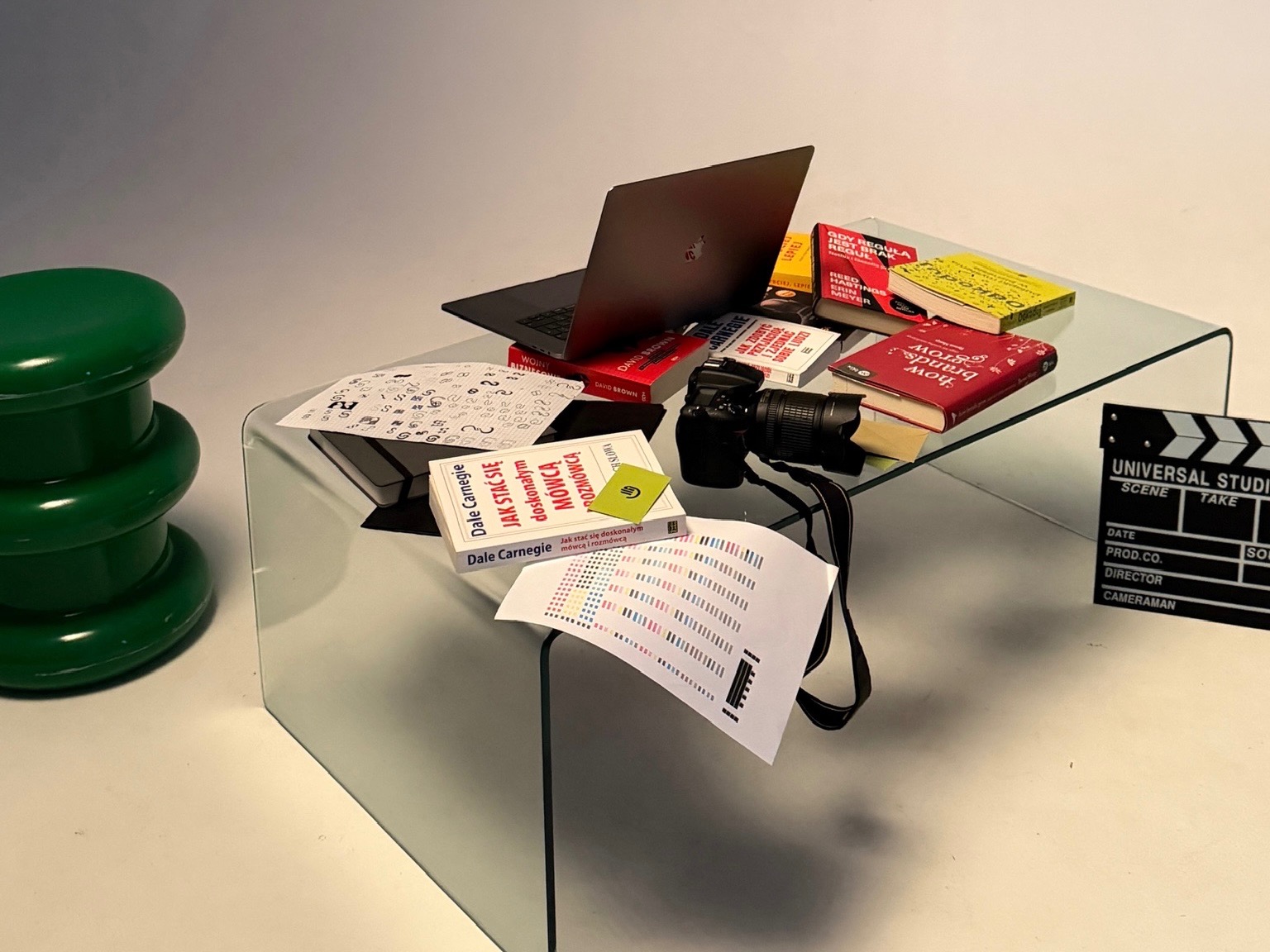 Kreatywne biurko z laptopem, aparatem, książkami o brandingu i rozwoju osobistym, oraz klapsem filmowym. Elementy graficzne i kolorystyczne na białym tle.