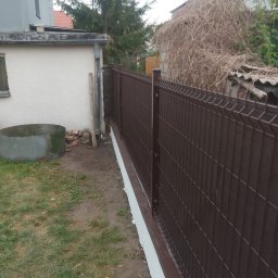 Marek Kaczmarczyk Maras Motors trans - Nowoczesne, brązowe ogrodzenie panelowe z podmurówką, oddzielające posesję. Widoczne elementy montażowe i słupki. W tle budynek i zieleń.
