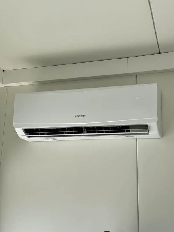 Biały klimatyzator Sinclair zamontowany na jasnej ścianie. Widoczny wyświetlacz temperatury. Minimalistyczny design, nowoczesne wnętrze.