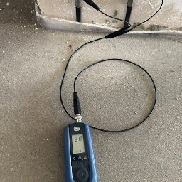 HydroTech Południe osuszanie po zalaniu, wynajem osuszaczy, likwidacja szkód po awari, lokalizacja wycieków - Miernik wilgotności w ścianie, wskazujący odczyt 87.0, z dwoma czujnikami wbitymi w ścianę. Pomiar wilgotności muru w trakcie osuszania.