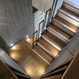 Iwona Cierpioł - Nowoczesne, drewniane schody z czarną, metalową balustradą, oświetlone punktowo, widziane z góry. Realizacja w Koninie.