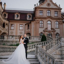 Miękka Sztuka Fotografia - Para młoda na tle zamku w Pszczynie. Panna młoda w białej sukni, pan młody w czarnym smokingu. Kamienne schody i balustrady. Romantyczna sesja ślubna.