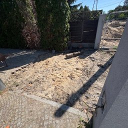 OSTROCLEAN - Teren po usunięciu kostki brukowej, widoczne pozostałości piasku i gruzu, ogrodzenie w tle. Przygotowanie do dalszych prac budowlanych.