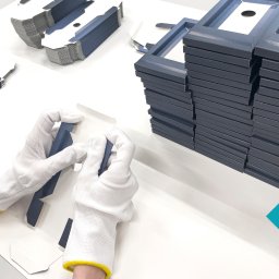 PURELLS INNOVATIVE SPÓŁKA Z OGRANICZONĄ ODPOWIEDZIALNOŚCIĄ - Ręczne pakowanie szarych, tekturowych ramek w białe pudełka, praca w sterylnych, białych rękawicach, stosy gotowych opakowań w tle. Precyzyjne pakowanie ręczne.