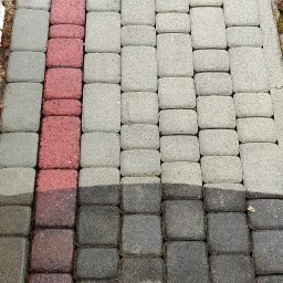 Pan Lanca Mycie Wysokociśnieniowe - Kostka brukowa podzielona na trzy pionowe sekcje: brudna i mokra, częściowo oczyszczona oraz czysta, sucha, jasnoszara, z trawą w tle.