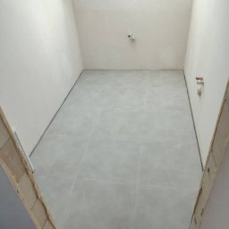 P&N Ceramo - Jasne, kwadratowe płytki podłogowe w małej łazience, widok z góry. Przygotowane ościeżnice drzwiowe. Minimalistyczny styl, świeżo po remoncie.
