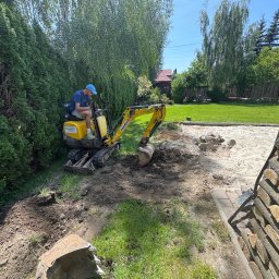 Weaver - Żółta mini koparka w akcji na działce, operator w niebieskiej czapce. Wykop pod piaskownicę z drewnianym obrzeżem, trawa, drzewa w tle.