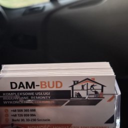 DAM-BUD - Wizytówki firmy DAM-BUD w przezroczystym podajniku, oferującej kompleksowe usługi budowlane, remonty, wykończenia i elewacje. Nowość: montaż stolarki okiennej i umywalki z płytek.