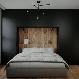 Arkush - Nowoczesna sypialnia z drewnianym zagłówkiem, czarnymi szafami w zabudowie i designerską lampą sufitową. Minimalistyczny wystrój z akcentami drewna i betonu.