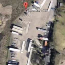 Widok z lotu ptaka na plac składowy z naczepami ciężarówek, oznaczony czerwoną pinezką lokalizacyjną 'Aleksandra Ostrowskiego 102'.