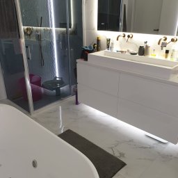 KRDM - Nowoczesna łazienka z kabiną prysznicową, białą szafką pod umywalką z podświetleniem LED i wanną. Marmurowe płytki podłogowe i złote baterie.