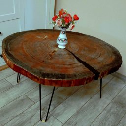 WoodCreft Zgarda - Stolik kawowy z litego drewna z wyraźnym pęknięciem wypełnionym czarną żywicą epoksydową, na metalowych nogach typu hairpin, z wazonem z kwiatami na blacie.