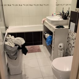 Royal Clean - Przed sprzątaniem: przepełniony kosz na pranie w łazience z białą armaturą i brązowymi akcentami. Widoczna wanna, umywalka z akcesoriami i toaleta.