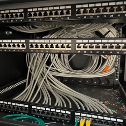Michał Gandyk - Panel krosowniczy Cat.6A z kablami sieciowymi w szafie rack. Widoczne porty RJ45, oznaczenia numerów i kolorowe kable patchcord. Detal instalacji sieci komputerowej.