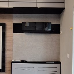 Air Construction - Nowoczesny, czarny klimatyzator ścienny AUX, zamontowany w salonie nad szarą szafką z ażurowymi drzwiczkami. Szare szafki wiszące pod sufitem.