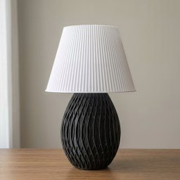 SHOFL - Stylowa lampka nocna z czarną, ażurową podstawą i białym, plisowanym abażurem, stojąca na drewnianym blacie. Neutralne tło, delikatne światło.