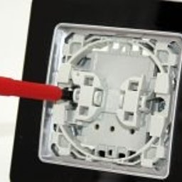 TEDENET - Grupa Smart - Montaż gniazdka elektrycznego z czarną ramką, widok z bliska, narzędzia w użyciu. Usługi elektryczne w Krakowie, precyzja i dbałość o detale.