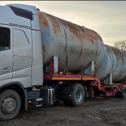 PTUH Jan Cieślik - Laweta Volvo FH 500 przewozi dwa duże, skorodowane zbiorniki na niskopodwoziowej platformie. Widoczne tablice rejestracyjne i teren poza drogą.