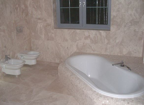 Jasna łazienka z marmurowymi płytkami, białą wanną, bidetem i toaletą pod oknem.