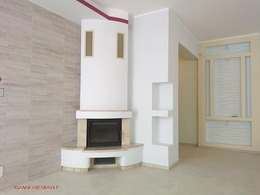 Nowoczesny salon z kominkiem obłożonym trawertynem, ściana z dekoracyjną okładziną imitującą kamień, minimalistyczne wnęki ścienne i ozdobna ścianka działowa z falistym wzorem.