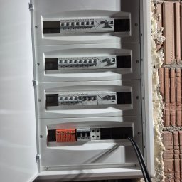 Elektryk Majkel Michał Środek - Otwarta, biała skrzynka rozdzielcza z bezpiecznikami EATON na ceglanej ścianie z pianką montażową. Widoczne przewody i zabezpieczenia.