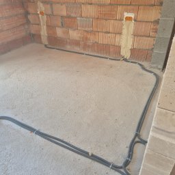 Elektryk Majkel Michał Środek - Wnętrze w trakcie prac: kable w peszlach ułożone wzdłuż ścian z cegły i betonu, mocowane klamrami do podłoża. Przygotowanie do instalacji elektrycznej w nowym budynku.