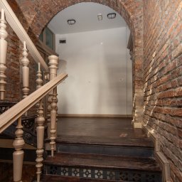 Villa.M - Klatka schodowa z ceglanym łukiem i drewnianymi schodami z dekoracyjnymi elementami. Widok z dołu na górę, oświetlenie górne.