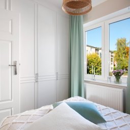 KMK Meble - Jasna sypialnia z białą szafą w zabudowie, widokiem na zieleń za oknem i dekoracyjnymi poduszkami na łóżku. Minimalistyczny design z akcentami natury.