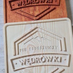 ABIKS Rafał Skiba - Dwie drewniane tabliczki z frezowanym napisem 'PUB PODRÓŻNICZY WĘDRÓWKI' i motywem górskim; jedna surowa, druga bejcowana na brązowo.