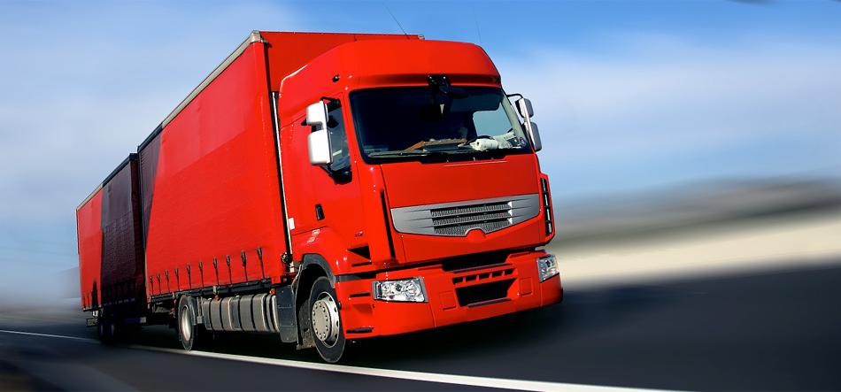 Czerwona ciężarówka z naczepą w ruchu, sfotografowana dynamicznie z niskiego kąta, z efektem rozmycia tła sugerującym dużą prędkość, na tle błękitnego nieba.