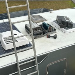 PRIMACOOL - Serwis klimatyzacji na dachu kampera: rozmontowana jednostka, wiertarka, drabina. Widoczne panele słoneczne i elementy instalacji. Prace w toku, widok z góry.
