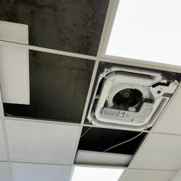 PRIMACOOL - Kasetonowy sufit z widoczną jednostką klimatyzacji kasetonowej w trakcie montażu lub serwisu. Widoczne przewody i elementy konstrukcyjne.