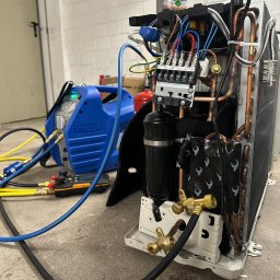 PRIMACOOL - Rozłożona jednostka klimatyzacji z podłączonym sprzętem serwisowym, widoczne przewody, złączki i elementy elektryczne. Sprzęt VALUE w tle.