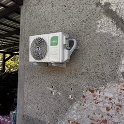 SB Elektro - Zamontowana jednostka zewnętrzna klimatyzacji Kaisai na szarej, chropowatej ścianie budynku z widocznymi fragmentami cegieł. Widoczne przewody i elementy montażowe.