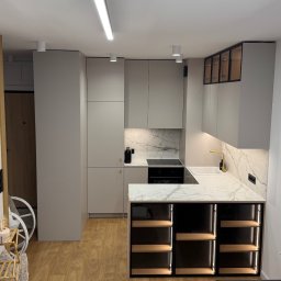 KoNad Group sp. z o.o. - Kompaktowa, szara kuchnia z marmurowym blatem i złotą armaturą. Dolne szafki z podświetlanymi półkami. Minimalistyczne oświetlenie sufitowe.