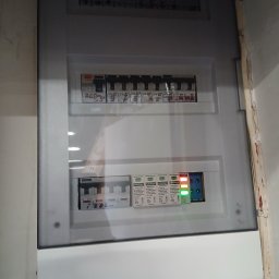 Usługi Elektryczne Aleksander Paszkow - Szara skrzynka rozdzielcza z bezpiecznikami i zabezpieczeniami w Zosin. Widoczne oznaczenia i diody sygnalizacyjne. Instalacja wewnątrz budynku.