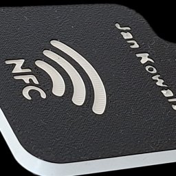 Brylok - Czarno-biały brelok NFC z imieniem 'Jan Kowalski', wykonany metodą addytywną. Widoczna tekstura materiału i warstwy. Otwór na kółko do kluczy.
