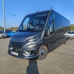 KLARIBUS DANIEL BRYL - Szary bus Iveco Daily z przyciemnianymi szybami, zaparkowany na parkingu z kostki brukowej w słoneczny dzień. Widoczny numer rejestracyjny W6 KLARI.