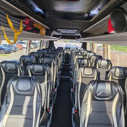 KLARIBUS DANIEL BRYL - Czyste wnętrze nowoczesnego autokaru z rzędami czarno-beżowych foteli, pikowaną podsufitką i słonecznym światłem wpadającym przez okna, ukazującym parking.