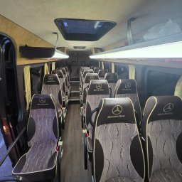 KLARIBUS DANIEL BRYL - Przestronne wnętrze minibusa Mercedes-Benz z rzędami wzorzystych foteli pasażerskich, oświetlone LED-ami, z otwartymi drzwiami i widokiem na ulicę.