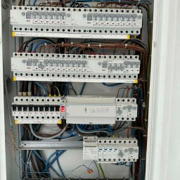 MW Elektro-System - Rozdzielnica elektryczna z bezpiecznikami EATON i Schneider, widoczne przewody, listwy zaciskowe z opisami 'DOM' i 'PODŁOGÓWKA', oświetlenie górne.