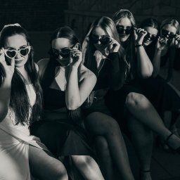 AGACEBULAFOTO - Czarno-białe zdjęcie grupy kobiet w okularach w kształcie serc, siedzących obok siebie. Jedna z nich ma welon. Ujęcie z dołu, podkreślające stylizacje.