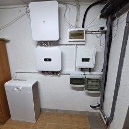 LILIANNA SOŁTAN Step by lili - Zainstalowany system fotowoltaiczny: dwa inwertery Huawei i Inversolar, magazyn energii Huawei LUNA2000 oraz skrzynki elektryczne na białej ścianie w pomieszczeniu technicznym.