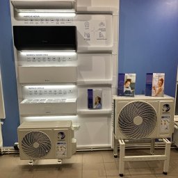INSTALBUD SYSTEM - Ekspozycja klimatyzatorów Nørdis: Nova, Orion Pro i Sirius. Modele w różnych kolorach i z różnymi funkcjami, prezentowane na białym panelu na tle niebieskiej ściany.