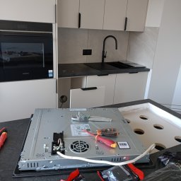 MA-Elektro - Podłączenie płyty indukcyjnej Siemens w nowoczesnej kuchni. Widoczne narzędzia, przewody i otwór w blacie. Ujęcie z bliska, z perspektywy osoby montującej.