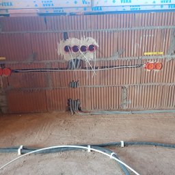 MA-Elektro - Ściana z cegły dziurawki z puszkami i przewodami w trakcie prac w Jemielnicy. Widoczne kable i peszle. Etap instalacji przed tynkowaniem.