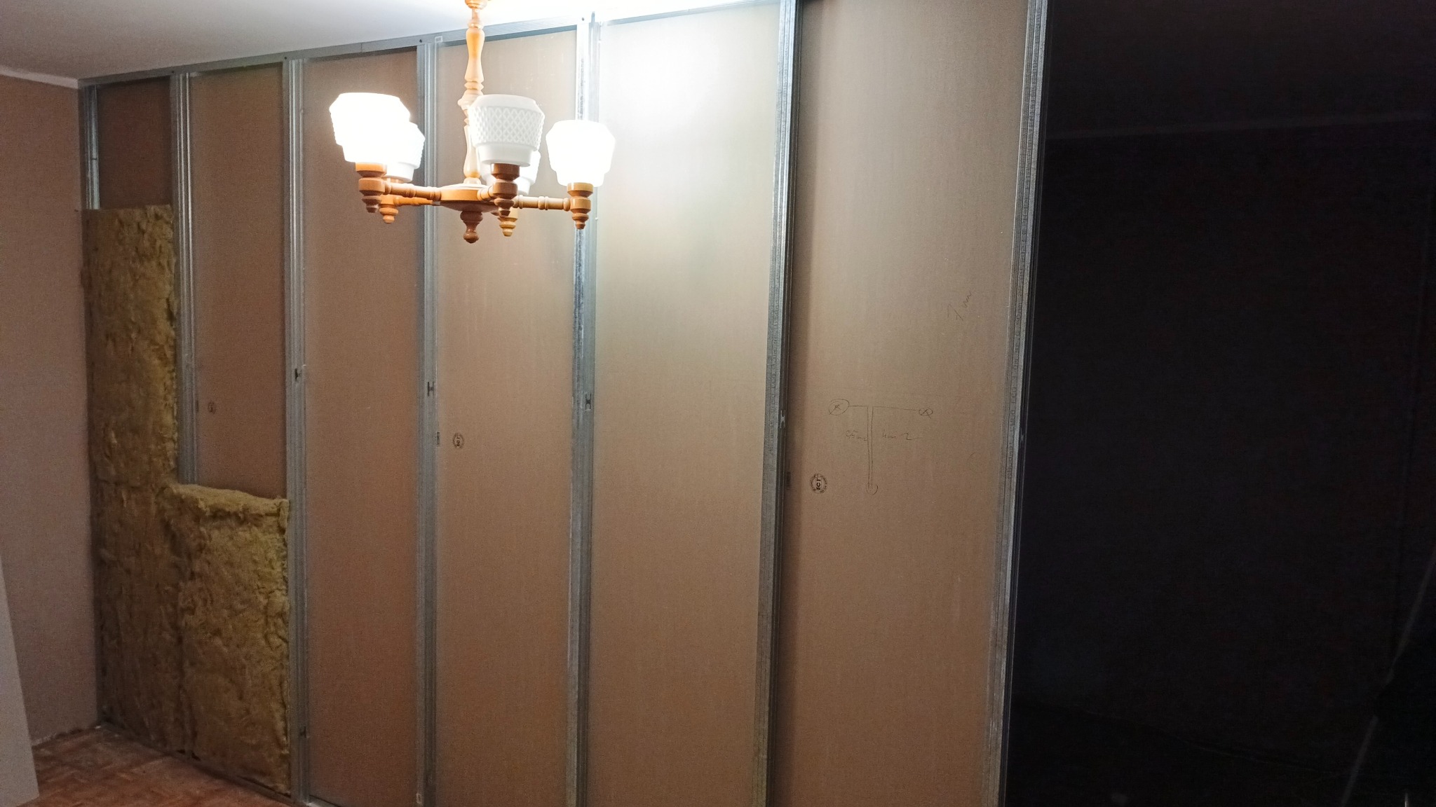 Montaż ścian działowych: metalowy szkielet z częściowo zamontowaną izolacją z wełny mineralnej, widoczne płyty kartonowo-gipsowe i wisząca lampa.